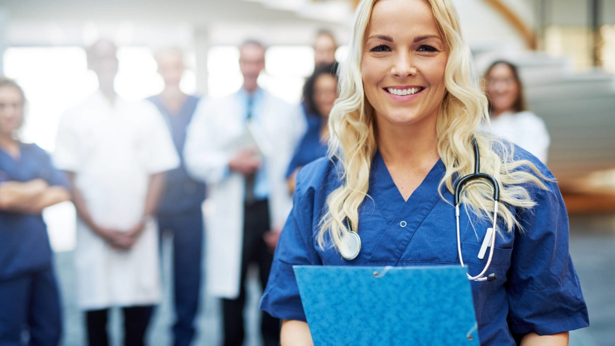 Smiling young blond woman in uniform standing in a hospital with the papers.