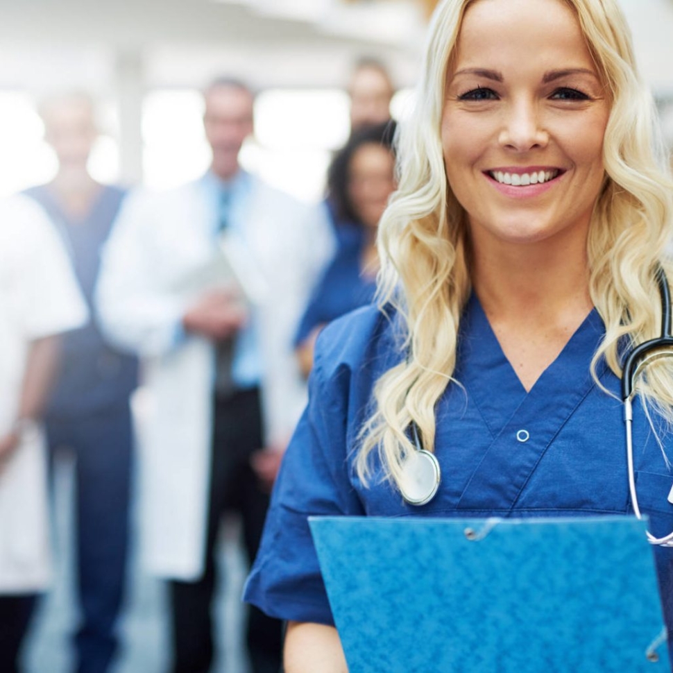 Smiling young blond woman in uniform standing in a hospital with the papers.